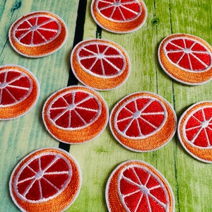 Könnte beinhalten: Zehn gestickte Bügelbilder in Form einer Grapefruit. Die Patches sind orange mit einem weißen Umriss und einer roten Grapefruit im Inneren.
