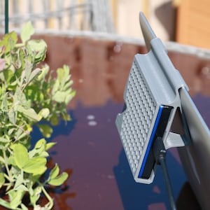 May include: A gray 3D printed hard drive enclosure with a blue USB cable attached to a laptop. The enclosure has a textured surface and is attached to the laptop with a clip.