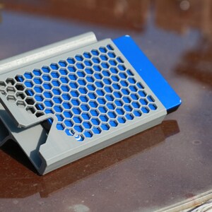 May include: A gray 3D printed stand with a honeycomb design holds a blue hard drive.