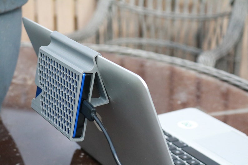 May include: A gray laptop stand with a honeycomb design and a blue external hard drive attached to it. The hard drive is connected to the laptop with a black cable.
