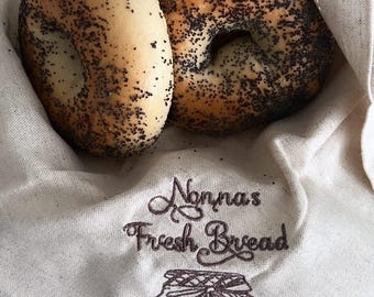 Puede incluir: Tres bagels de semillas de amapola en una bolsa de tela blanca con el texto "Nonna's Fresh Bread" y un dibujo de un frasco con una etiqueta que dice "Sour Dough".