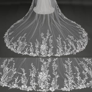 May include: A long, white bridal veil with intricate floral embroidery. The veil features delicate, detailed patterns of flowers and foliage along the edges, creating an elegant and romantic look. The sheer fabric allows for a soft, flowing drape.