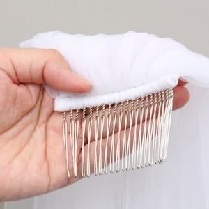 May include: A white bridal veil with a comb attached. The veil is made of a sheer, lightweight fabric. The comb has silver-colored metal teeth.