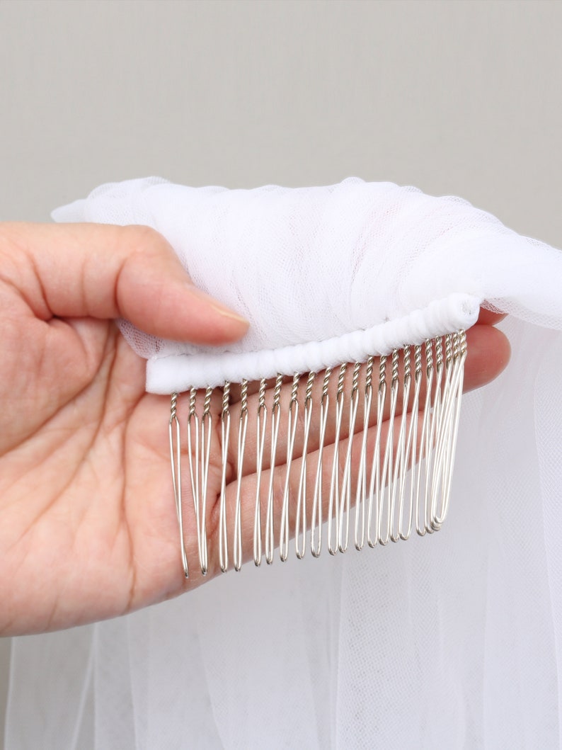 May include: A white bridal veil with a comb attached. The veil is made of a sheer, lightweight fabric. The comb has silver-colored metal teeth.