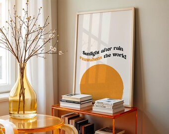 May include: A framed art print with the text "Sunlight after rain reawakens the world" above a large orange circle. The print is displayed on a clear orange shelf with books. A yellow vase holds branches with small white flowers.