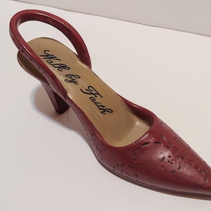 May include: A red high-heeled shoe with a slingback strap and a cutout design. The insole is tan and reads "Walk by Faith".