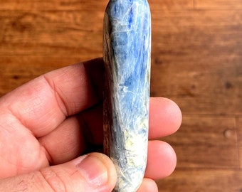 May include: A smooth, polished blue kyanite crystal with a light blue and white striated pattern. The crystal is shaped like a long, thin oval.