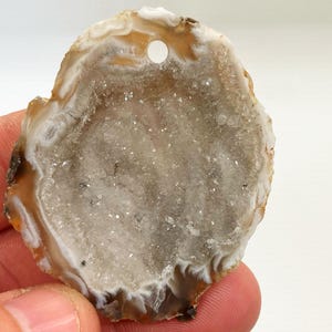 May include: A natural agate slice with a hole drilled through the top. The agate is brown and white with a clear, crystal-like center.
