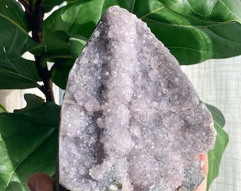 Könnte beinhalten: Ein großer, violetter Amethyst-Kristallcluster mit einer natürlichen, rauen Außenseite. Der Kristall ist hellviolett und hat eine glatte, polierte Oberfläche. Der Kristall ist eine beliebte Wahl für Meditation und Heilung.