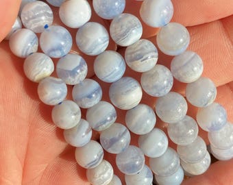 May include: A strand of blue lace agate beads, with a light blue and white banded pattern, is shown in a hand. The beads are round and smooth.