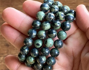 May include: A stack of green and black gemstone bracelets. The beads are round and have a marbled pattern.