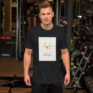 Peut inclure: T-shirt gris foncé avec une illustration à l'aquarelle d'un chien Poméranien. L'image comprend le texte "Born cute. Stayed superior." Le t-shirt est fait d'une matière douce et convient aux tenues décontractées.
