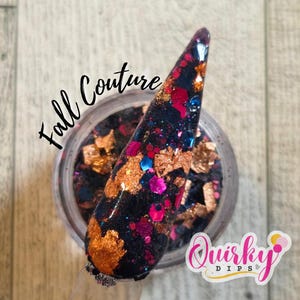 May include: A nail swatch with a dark base, adorned with gold, pink, and blue glitter and flakes. The words "Fall Couture" are written in cursive. The jar of nail dip powder is visible, with the "Quirky Dips" logo.