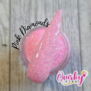 Könnte beinhalten: Ein Tiegel mit rosa Nagel-Dip-Puder mit Glitzer-Finish. Ein klarer Nagel-Swatch wird in das Puder getaucht, um die Farbe und Textur zu zeigen. Die Wörter "Pink Diamonds" und "Quirky Dips" sind sichtbar.