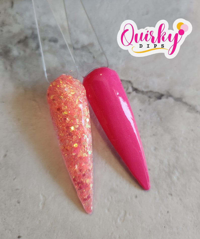 May include: Two nail dip samples, one is a pink glitter and the other is a solid hot pink. The samples are on a white surface with the text "Quirky Dips" in a white circle with a pink outline.