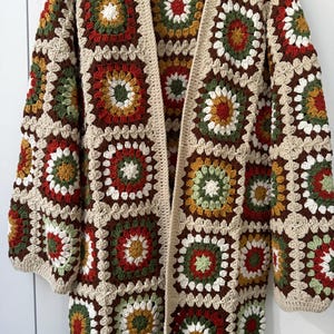 Könnte beinhalten: Eine gehäkelte Strickjacke mit einem Granny-Square-Muster in Braun-, Rot-, Grün- und Weißtönen.