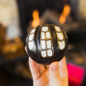 May include: A black and white decorative sphere with gold accents. The sphere is made of wood and has a carved design.
