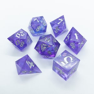 May include: Set of seven purple and silver dice with iridescent glitter. The dice are numbered 1 through 6 and include a d4.