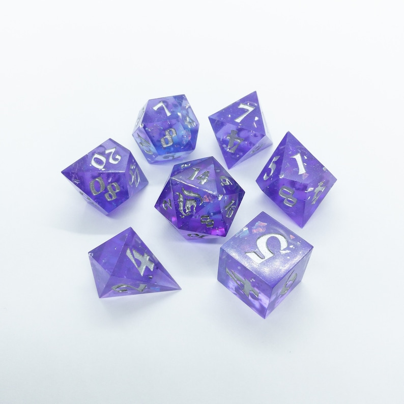 May include: Set of seven purple and silver dice with iridescent glitter. The dice are numbered 1 through 6 and include a d4.