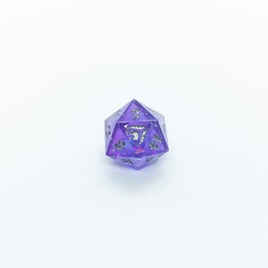 May include: A purple and silver iridescent d20 dice with a galaxy design. The dice is a 20-sided die used in tabletop role-playing games.