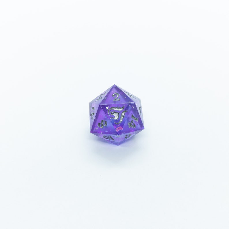 May include: A purple and silver iridescent d20 dice with a galaxy design. The dice is a 20-sided die used in tabletop role-playing games.