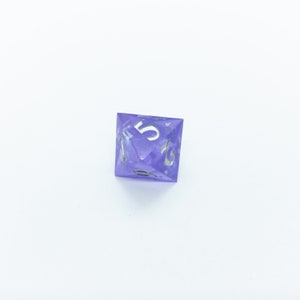 May include: A purple, iridescent, six-sided dice with silver numbers. The dice shows the number five.