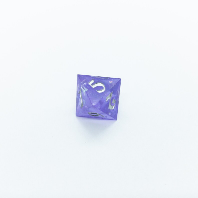May include: A purple, iridescent, six-sided dice with silver numbers. The dice shows the number five.
