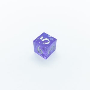 May include: A purple, translucent dice with white numbers. The dice is showing the number 5.