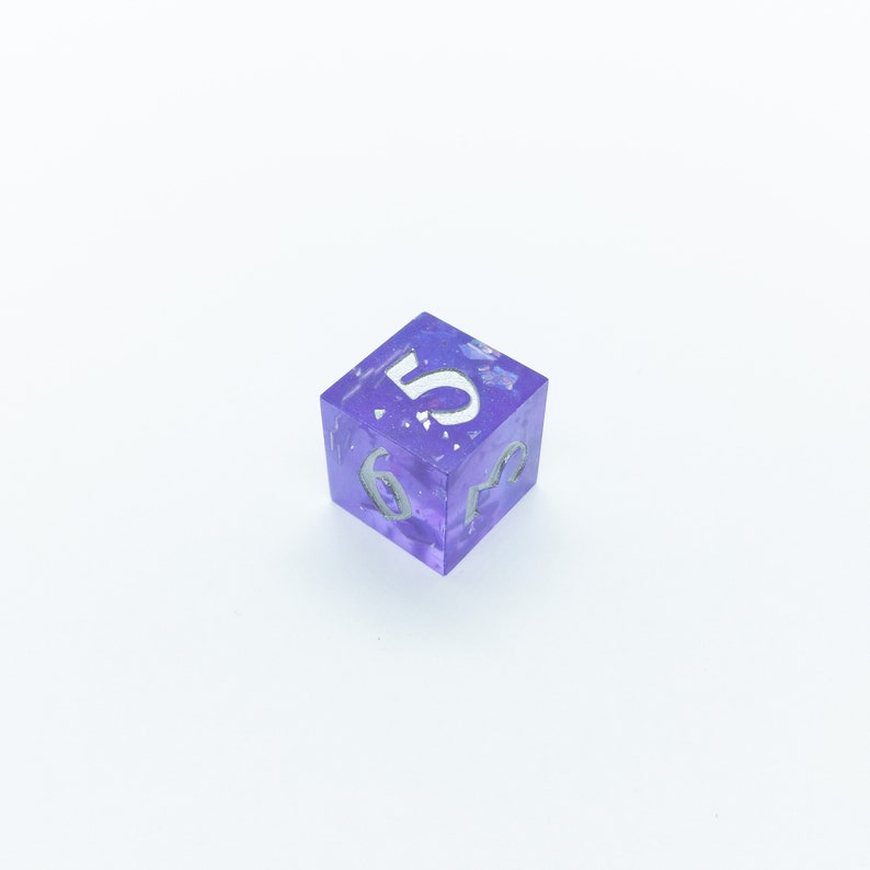 May include: A purple, translucent dice with white numbers. The dice is showing the number 5.
