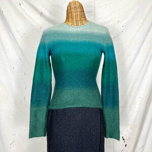 May include: A long-sleeved, green and blue ombre sweater with a crew neck. The sweater is made of a soft, fuzzy material.
