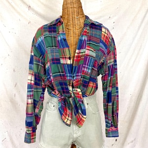 Könnte beinhalten: Langärmliges kariertes Hemd im Patchwork-Design mit einer Mischung aus grünen, blauen, roten und violetten Quadraten. Das Hemd ist an der Taille gebunden und zeigt einen lässigen Vintage-Stil. Es hat einen Kragen und geknöpfte Manschetten.
