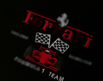 May include: Black crew neck t-shirt with red embroidered "Ferrari" text and a Formula 1 race car design. Features checkered flags and the text "Formula 1 Team".