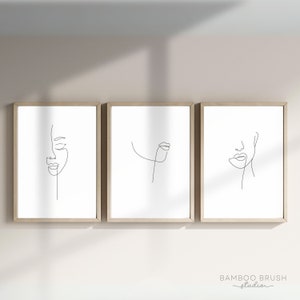 Op de afbeelding: Drie ingelijste minimalistische lijntekeningen van gezichten. Elke print toont een enkele lijntekening van een gezicht met verschillende accenten. De prints zijn in eenvoudig zwart en wit en zijn geplaatst tegen een witte achtergrond.