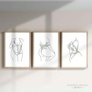 May include: Three minimalist line art prints of a person in a swimsuit with green foliage. The prints are framed in a light wood frame.
