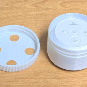 May include: White plastic sound machine with a circular control panel featuring four buttons and the text "transcend". The sound machine is accompanied by a separate white plastic base with four circular openings.