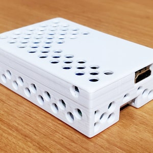 May include: A white plastic case with a honeycomb pattern for a Raspberry Pi computer. The case has a cutout for an HDMI port.