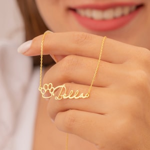 May include: Gold necklace with a paw print charm and the name "Bella" written in cursive.