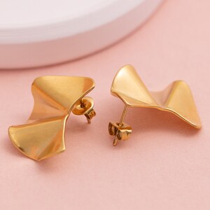 May include: A pair of gold-toned earrings with a wavy, asymmetrical design. The earrings are made of metal and have a post-back closure.