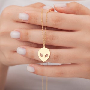 May include: A gold chain necklace with an alien head pendant. The pendant is a simple outline of an alien head with large eyes.