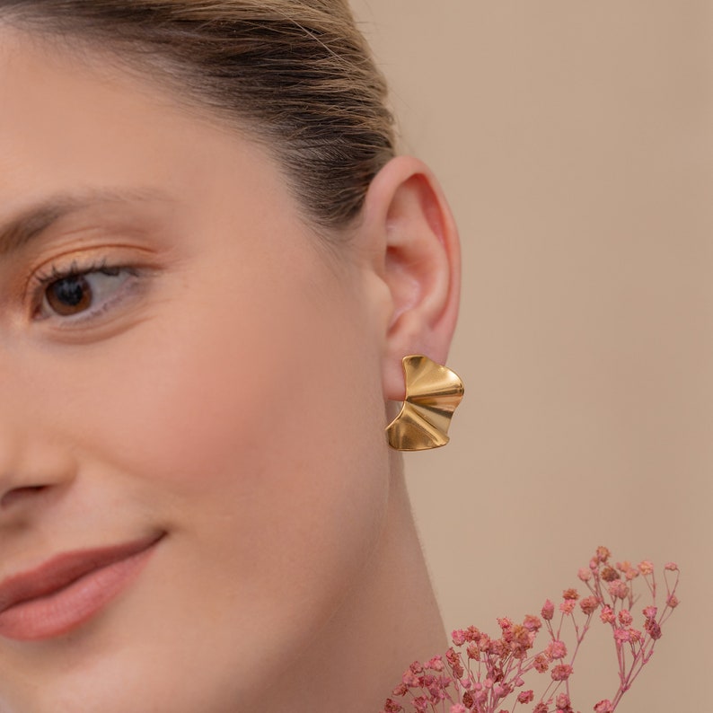 May include: A pair of gold-toned earrings with a unique, asymmetrical, fan-shaped design. The earrings are made of a smooth, textured metal.