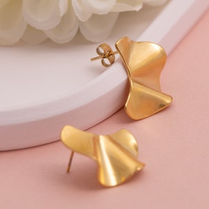 May include: A pair of gold-toned earrings with a wavy, asymmetrical design. The earrings are made of metal and have a polished finish.