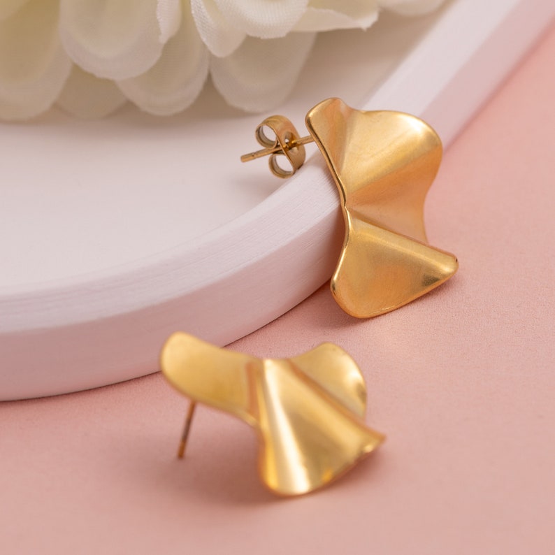 May include: A pair of gold-toned earrings with a wavy, asymmetrical design. The earrings are made of metal and have a polished finish.