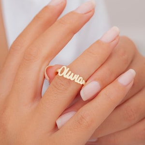 May include: A gold-toned ring with the name "Olivia" spelled out in cursive lettering.