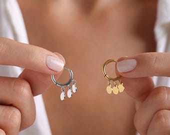 May include: Two hoop earrings with dangling charms. The earring on the left is silver with three silver charms. The earring on the right is gold with three gold charms.