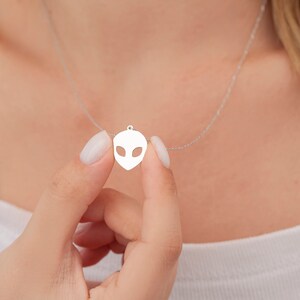Pu&ograve; includere: Una collana d'argento con un ciondolo a forma di testa aliena. Il ciondolo &egrave; un design a taglio, che mostra il viso dell'alieno con occhi grandi.