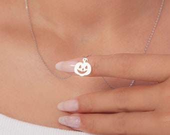 May include: A silver necklace with a small pumpkin charm. The charm is cut out in the shape of a pumpkin with a jack-o'-lantern face.
