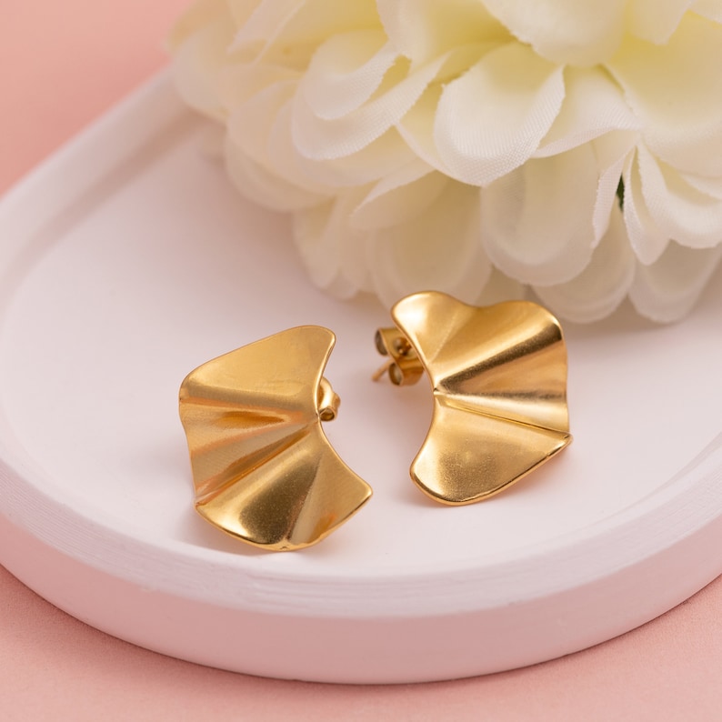 May include: A pair of gold-toned earrings with a wavy, ruffled design. The earrings are on a white surface.
