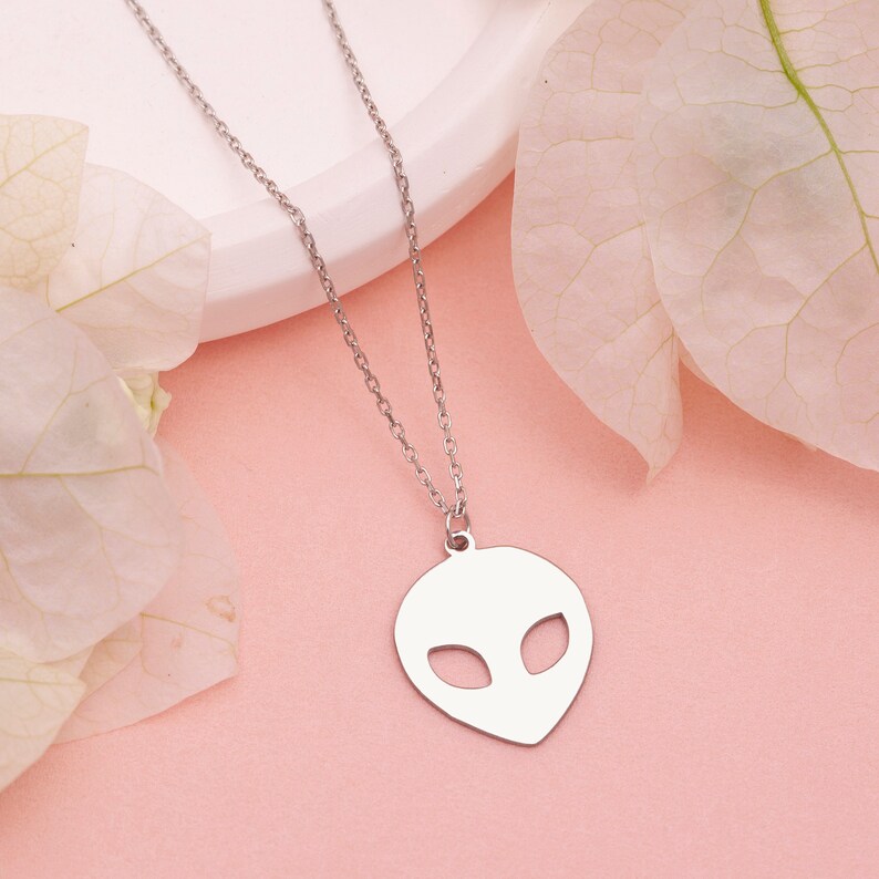 Pu&ograve; includere: Una collana con catena d'argento con un ciondolo a forma di testa aliena. Il ciondolo &egrave; un semplice contorno di una testa aliena con occhi grandi.