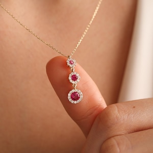 May include: A gold necklace with a pendant featuring three red ruby stones surrounded by smaller diamonds.