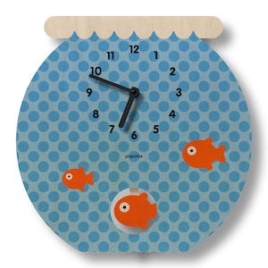 May include: A whimsical fishbowl-shaped wall clock. The clock face is light blue with a polka dot pattern and features three orange fish. Black clock hands indicate the time. The clock has a wooden top and the brand name "popclox" is printed on the face.